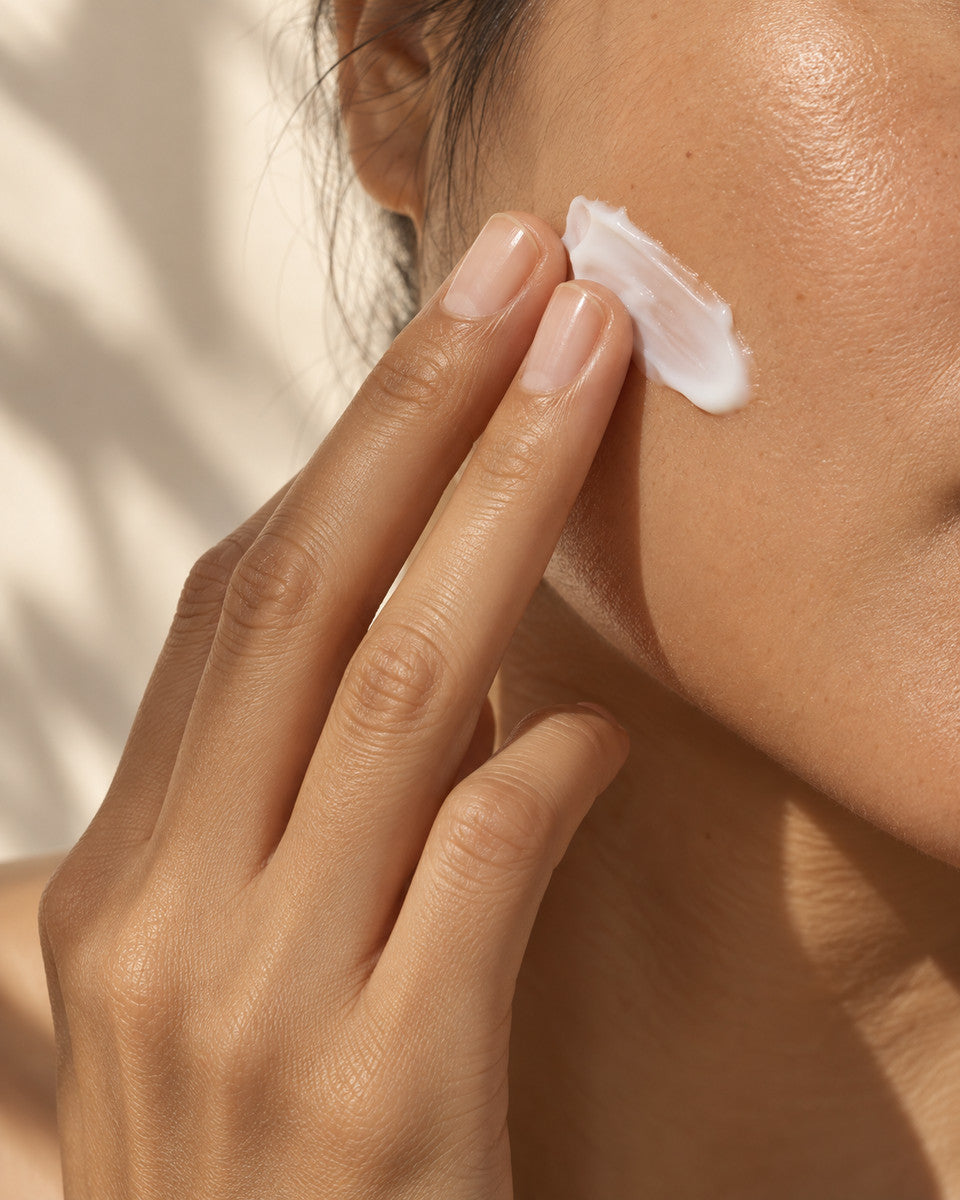 A close-up of white skincare cream being smoothed onto a cheek